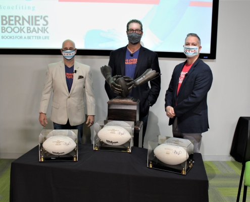 Three masked people stand in front of signed white footballs