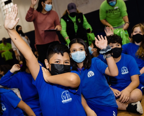 children wearing blue Saint Ann School school shirts raise their hands