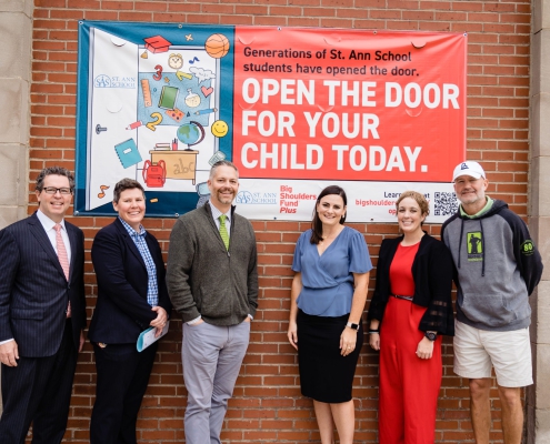 six Bernie's Book Bank workers pose in front of a banner that reads Generations of Saint Ann School student have opened the door, open the door for your child today