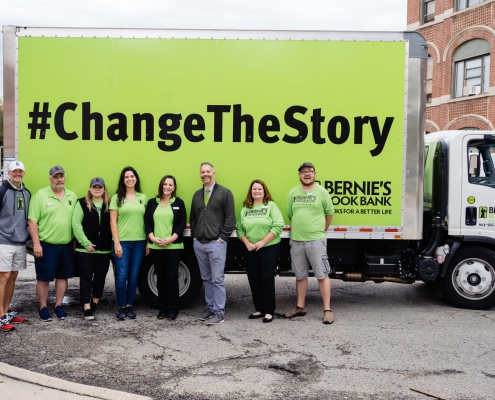eight volunteers smile in front of a green Bernie's Book Bank truck with the text # Change The Story