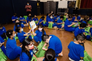 children sit on the floor and look through the books in their green Bernie's Book Bank bags