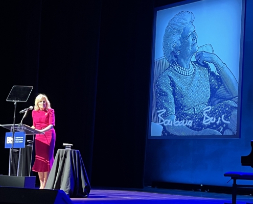 a speaker at a podium before a projected image of Barbara Bush