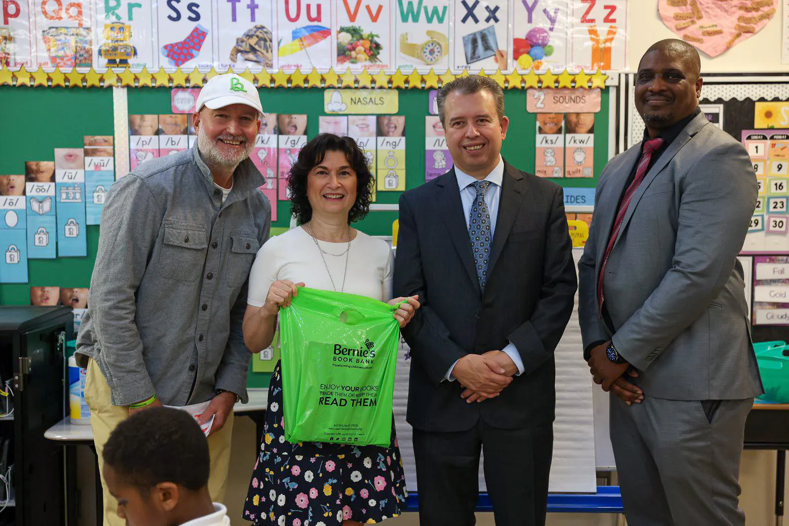 four adults pose and smile with a Bernie's Book Bank bag