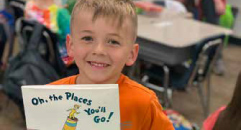 a child smiles and holds a copy of Oh the Places You'll Go