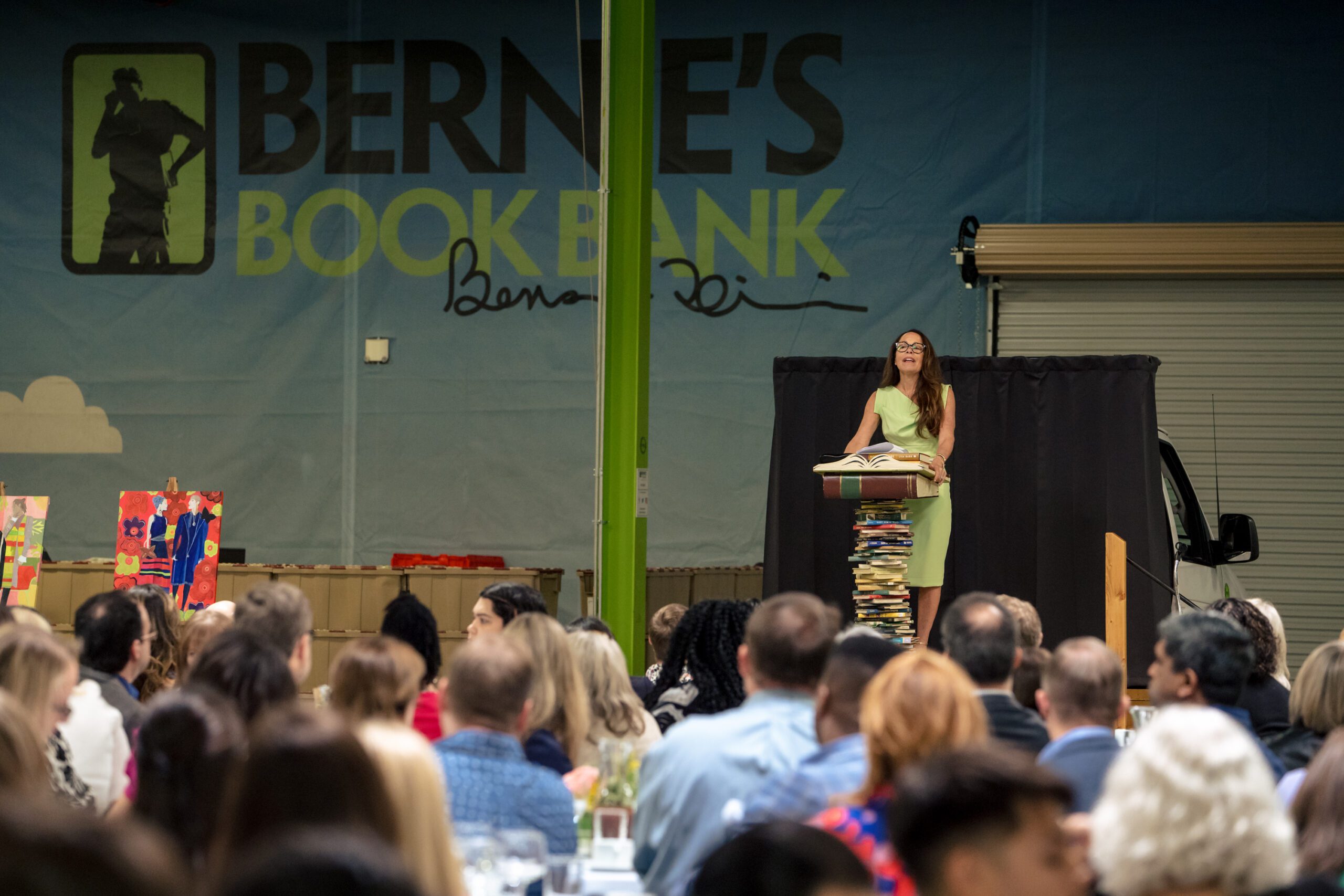a speaker at a podium made from a stack of books addresses a large crowd for Bernie's Book Lovers Lunch