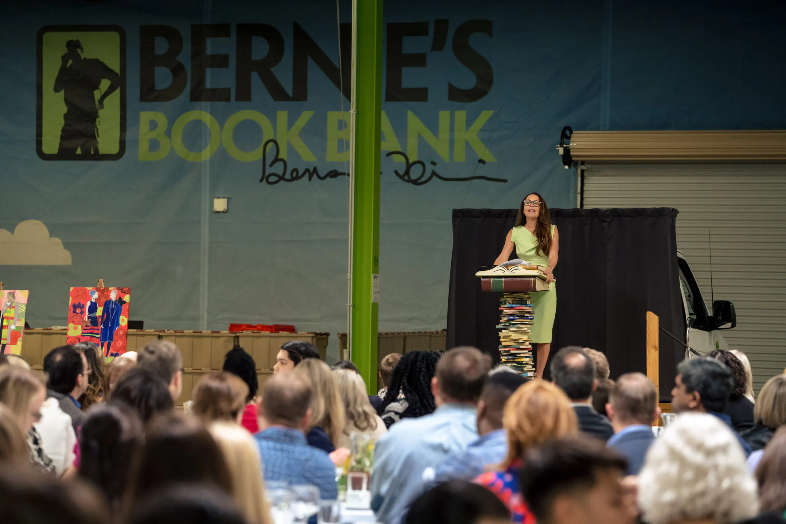 a speaker at a podium made from a stack of books addresses a large crowd for Bernie's Book Lovers Lunch
