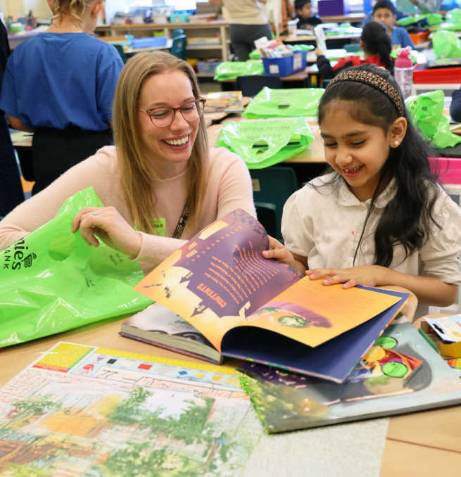 a grownup and child smile while paging through a pile of books