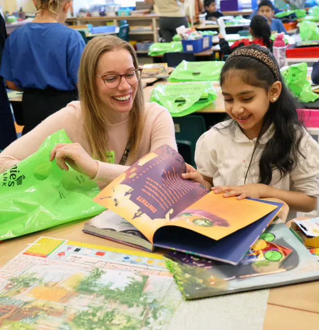 a grownup and child smile while paging through a pile of books