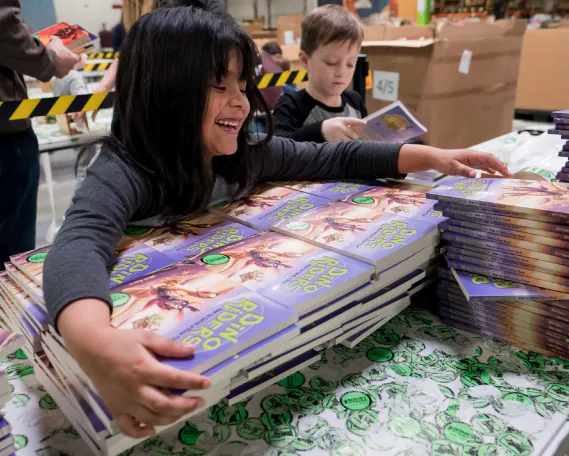 a kid happily clutches a stack of Dino Riders books