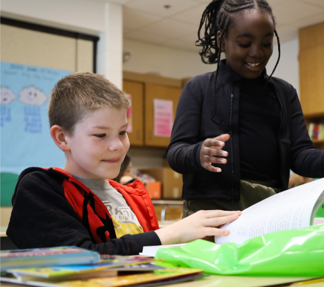 two schoolchildren smile and page through books