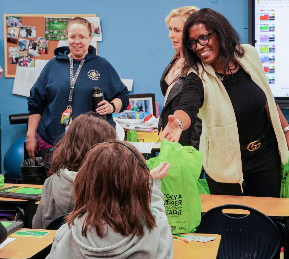 teachers and volunteers happily hand out books to a classroom of kids