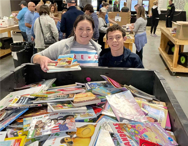 an adult and kid smile in front of a huge cardboard box filled with donated books