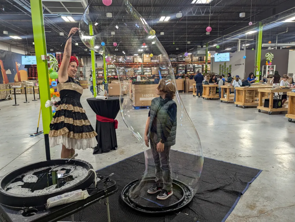 a performer uses a massive bubble wand to encircle a child at Booksgiving