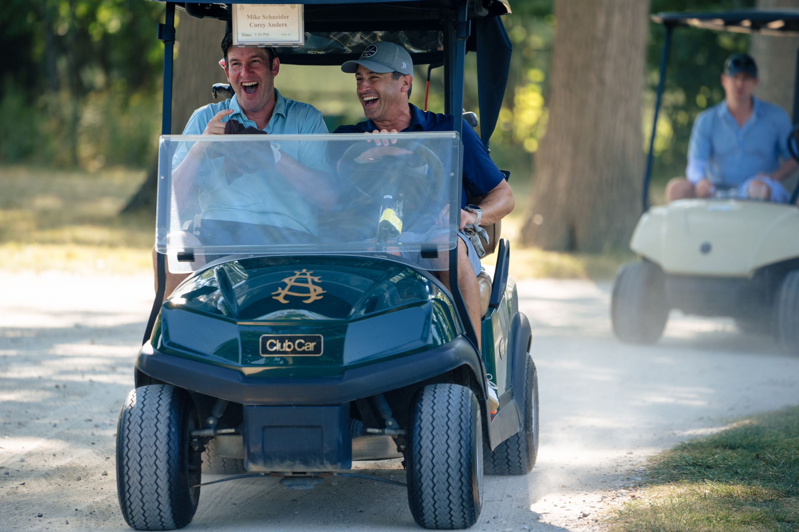 two male golfers laugh while riding in a cart