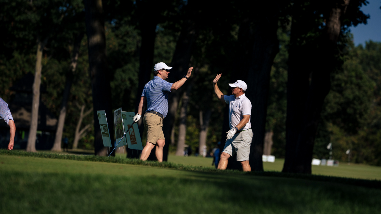 Two male golfers approach each other on the green, hands raise to high five each other