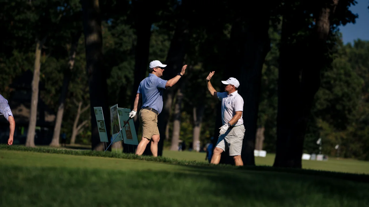 Two male golfers approach each other on the green, hands raise to high five each other