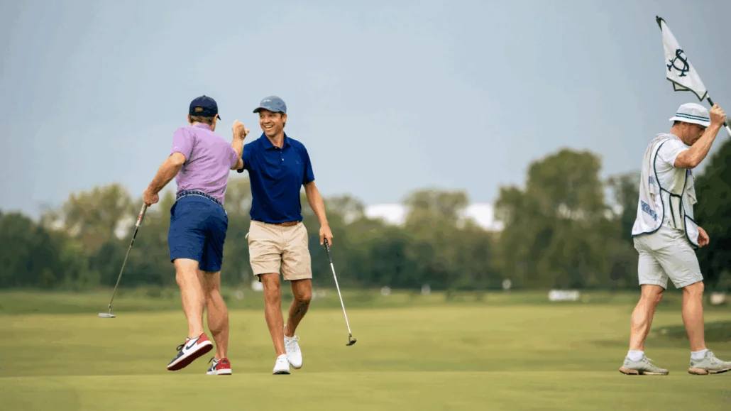 Two male golfers clasp hands enthusiastically on a sunlit green