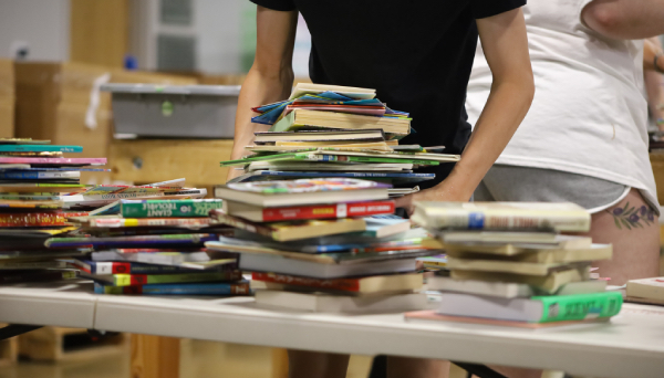 A volunteer grabs a tall stack of books from a table