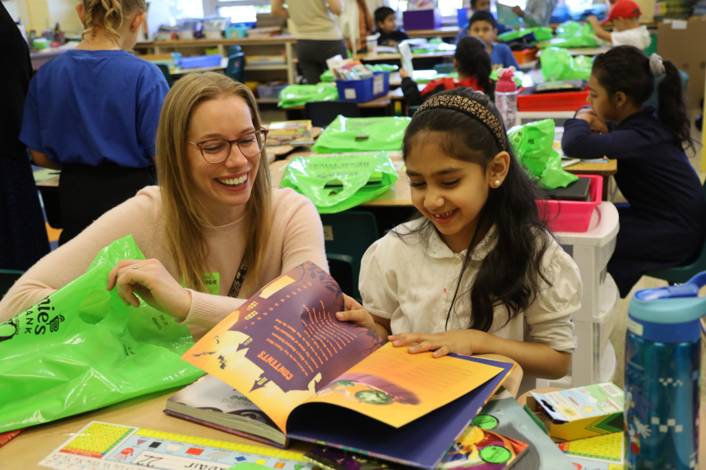 a grownup and child smile while paging through a pile of books