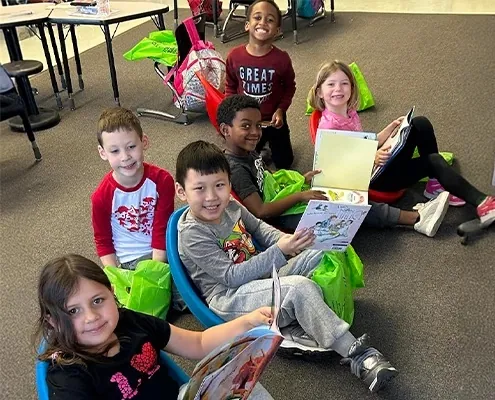 School kids sit on a classroom floor and smile with their donated picture books