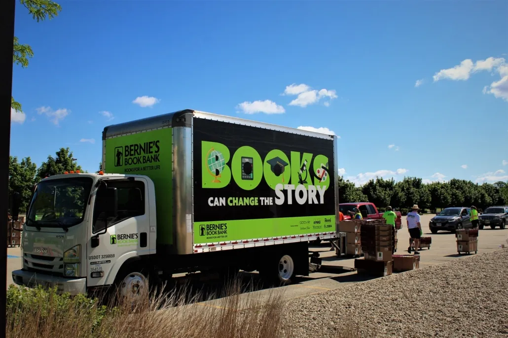 volunteers load boxes of books into a Bernie's truck parked in a sunlit parking lot; the side of the truck reads: books can change the story