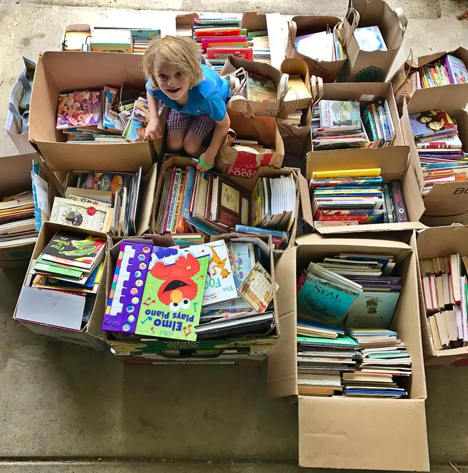 James (a smiling kid) sits amongst boxes and bags of hundreds of donated books