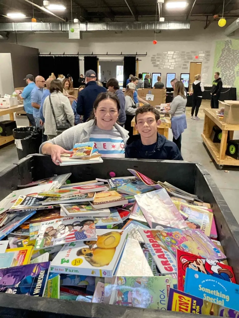 an adult and child smile in front of a large bin of donated picture books