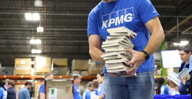 blue-shirted adult volunteers from K P M G sort stacks of books