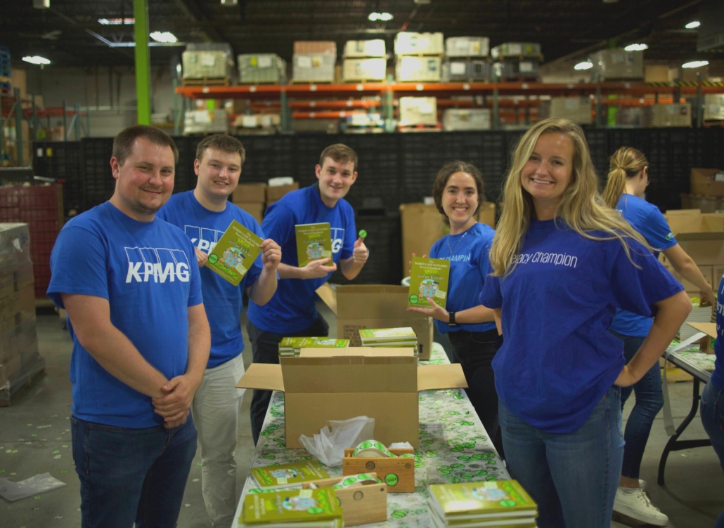 six volunteers from KPMG smile while boxing and organizing books