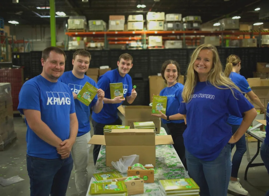 six volunteers from KPMG smile while boxing and organizing books