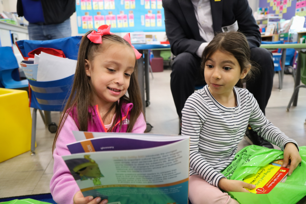 a schoolchild reads from a picture book to another kid, the two of them engaged and excited