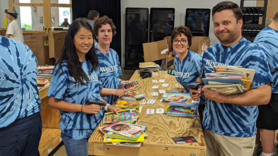 four blue-shirted volunteers from Wintrust Bank pack books at a large tablw