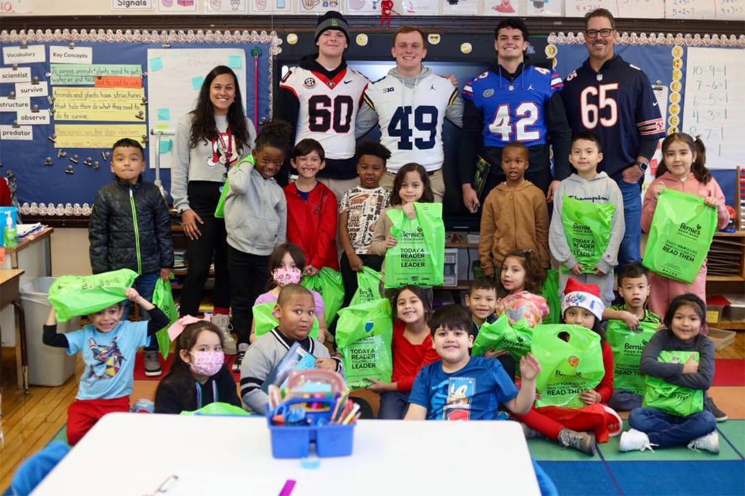 Group of football players posing for a picture with school kids in a classroom